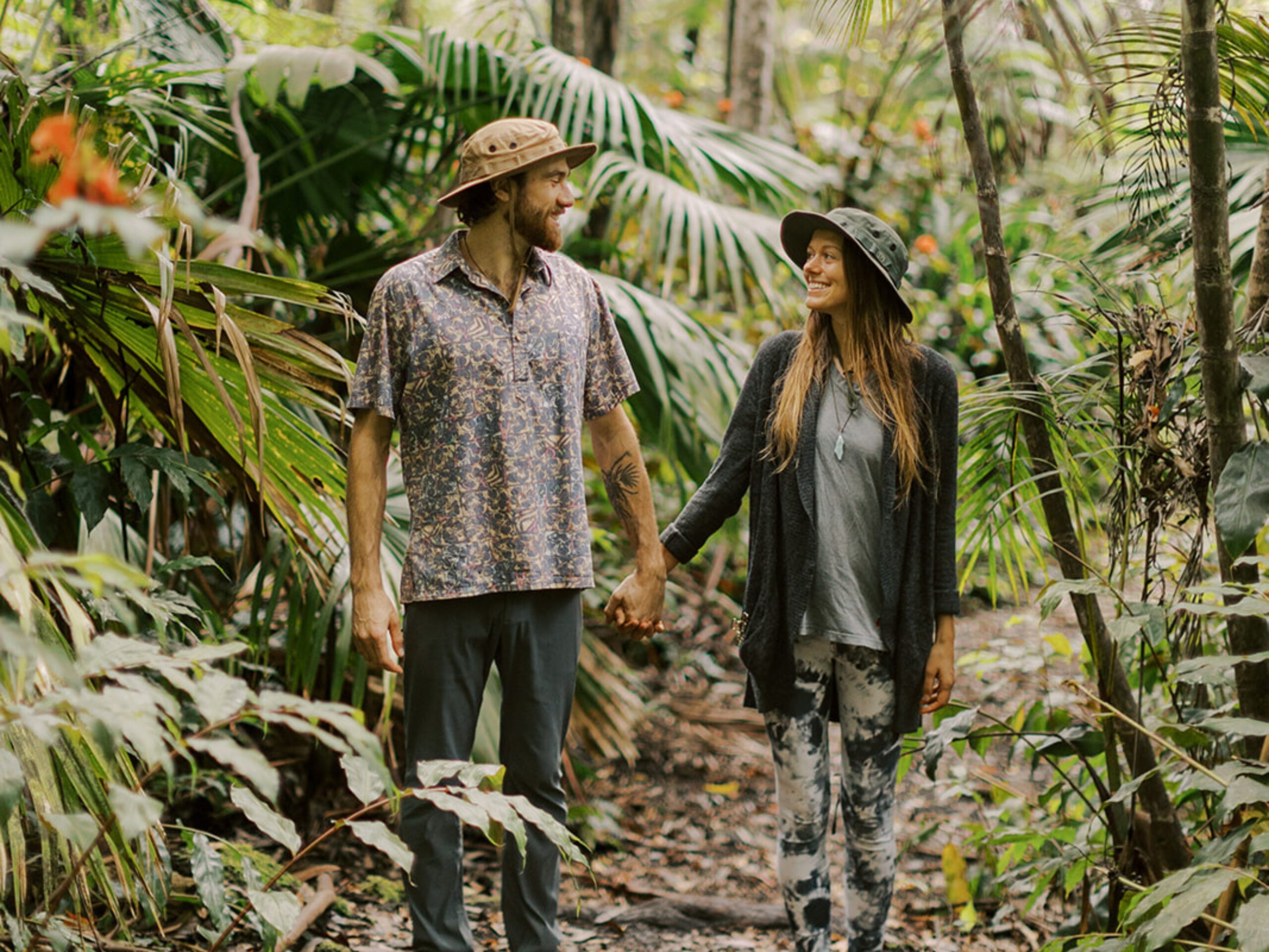 A couple walking through the forest holding hands.